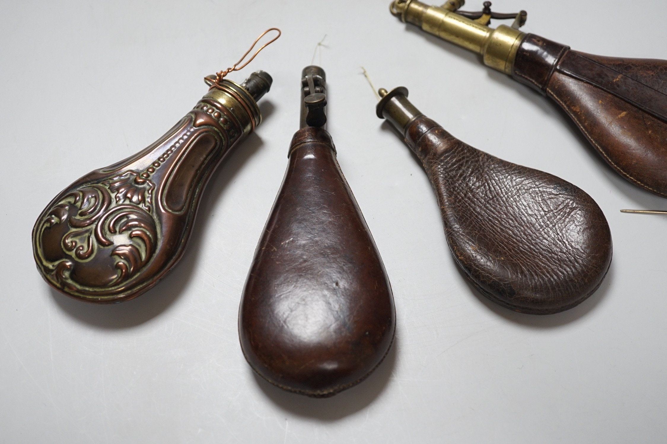 Four brass mounted powder flasks, to include three leather flasks, and one copper. Largest 24cm long